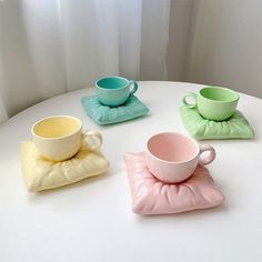 four different colored cups and saucers on a white table