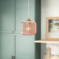 a pink glass light hanging from a ceiling in a room with green walls and cabinets