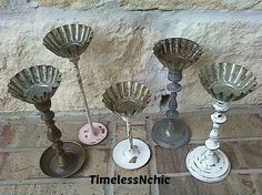 four metal candlesticks sitting next to each other on a tile floor in front of a stone wall