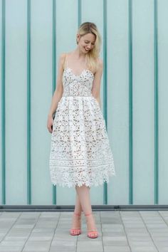 a woman standing in front of a blue wall wearing a white dress and pink shoes