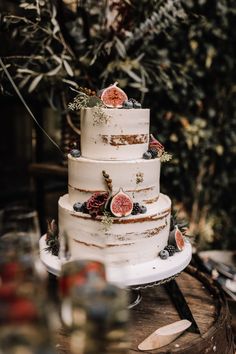 a three tiered cake with figs and berries on it sitting on a table