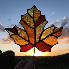 a hand holding a stained glass leaf at sunset