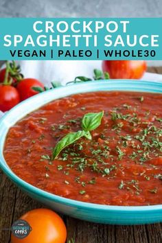 a bowl of crockpot spaghetti sauce with tomatoes and basil on the side in front of it