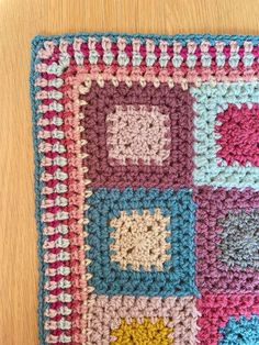 a crocheted square is shown on a wooden surface with the squares in different colors