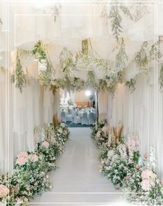 two tables with white linen covered chairs and flowers on the wall in front of them