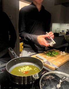 a man standing in a kitchen preparing food on top of a wooden cutting board next to pots and pans