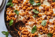 a pan filled with pasta and cheese covered in basil leaves on top of a table