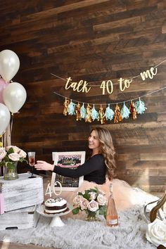 a woman sitting at a table with a cake and champagne in front of her, surrounded by balloons