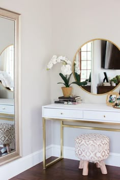 a white desk topped with a mirror and a small stool next to it on top of a hard wood floor