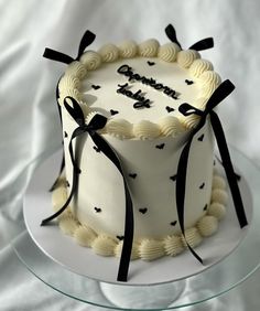 a white cake with black ribbon and bow decorations on the top is sitting on a glass plate