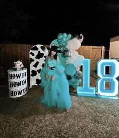 a woman in a blue dress standing next to a large number sign and cow balloons