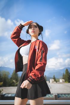 a woman in a red jacket and black skirt is posing for the camera with her hand on her head