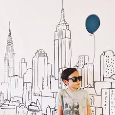 a young boy wearing sunglasses standing in front of a cityscape with a balloon