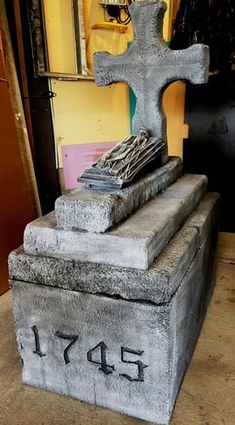 a cement grave with a cross and two books on it in front of a yellow wall