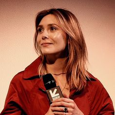 a woman in a red shirt holding a microphone and talking to someone on the other side