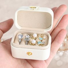 a person holding an open box with three rings in it and two pearls on the inside