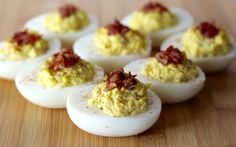 several deviled eggs with bacon on them sitting on a wooden table, ready to be eaten