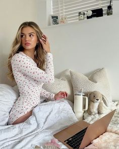 a woman is sitting on her bed and looking at the camera while using a laptop