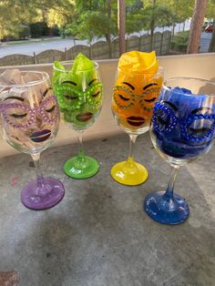 four wine glasses with masks on them sitting in front of a glass window sill