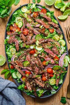 steak salad with tomatoes, cucumbers and onions on a platter next to a fork