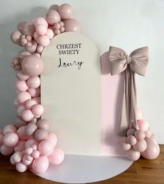 a white sign with pink balloons around it and a bow on the top of it