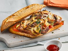 an open faced sandwich on a cutting board next to a bowl of ketchup