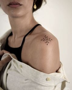 a woman with a small tattoo on her left shoulder and arm, holding onto a white shirt