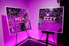 two large posters with writing on them in a purple lit room, one has a tripod stand and the other is a projection screen