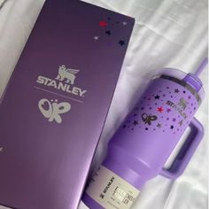 a purple travel mug sitting next to a box on a white sheet with the words stanley printed on it