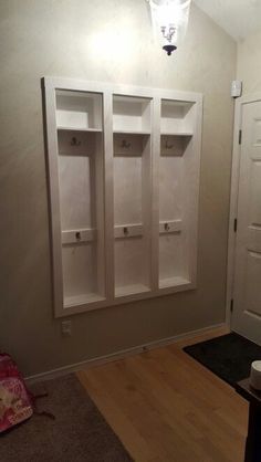 an empty room with two white shelves on the wall next to a door and a light above it