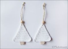 two crocheted christmas trees hanging from strings on a white surface with wood beads