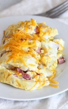 a white plate topped with an omelet covered in ham and cheese next to a fork