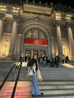 a woman is standing on the stairs in front of a building with columns and windows