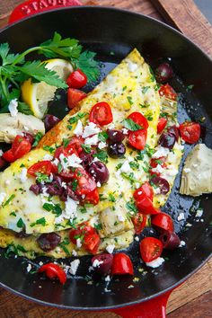 an omelet with tomatoes, olives and parsley in a skillet