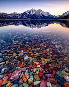 a lake with rocks in the water and mountains in the background at sunset or sunrise