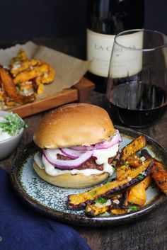 a plate with a sandwich and some fries on it next to a glass of wine