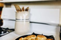 some biscuits are on a black plate on the stove top next to a mug and utensils