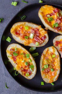 four loaded baked potatoes on a black plate with green onions and bacon in the middle