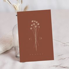 there is a card with flowers in it on the table next to a glass vase