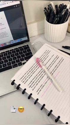 an open notebook sitting on top of a desk next to a laptop computer and pen