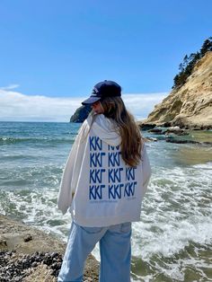 a woman standing on top of a beach next to the ocean wearing a white jacket