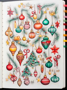 an open notebook with christmas ornaments on it and colored pencils in front of it