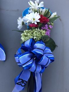 a blue ribbon tied around a vase filled with white, red and purple flowers on top of a gray wall