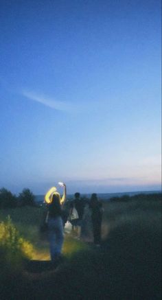 a group of people standing on top of a lush green field under a blue sky