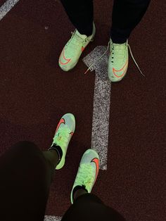 two people standing in the middle of a tennis court wearing green and orange nike shoes