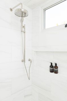 a shower head with two soap dispensers next to it in a white tiled bathroom