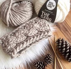 two balls of yarn and pine cones on top of a wooden table with knitting needles