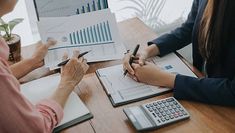 three people sitting at a table with papers and calculators