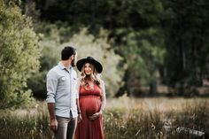 a pregnant woman in a red dress standing next to a man wearing a cowboy hat