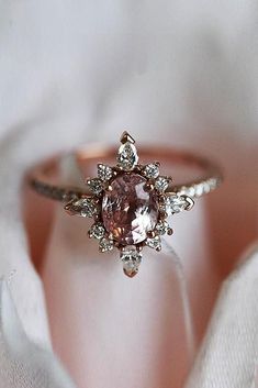 a pink diamond ring sitting on top of a white satin covered cloth with an open rose